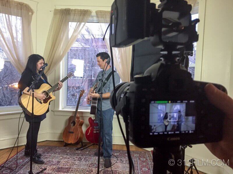 A man and a woman playing guitars in front of a camera