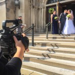 A cameraman filming a bride and groom on the steps of a church