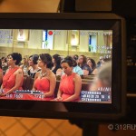 A camera recording a group of women in red dresses