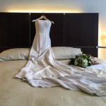 A wedding dress on a bed with a bouquet of flowers
