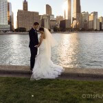 A bride and groom standing next to a body of water
