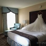 A wedding dress hanging on a bed in a hotel room