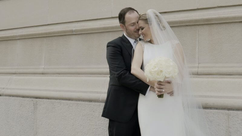 A bride and groom embracing each other in front of a building