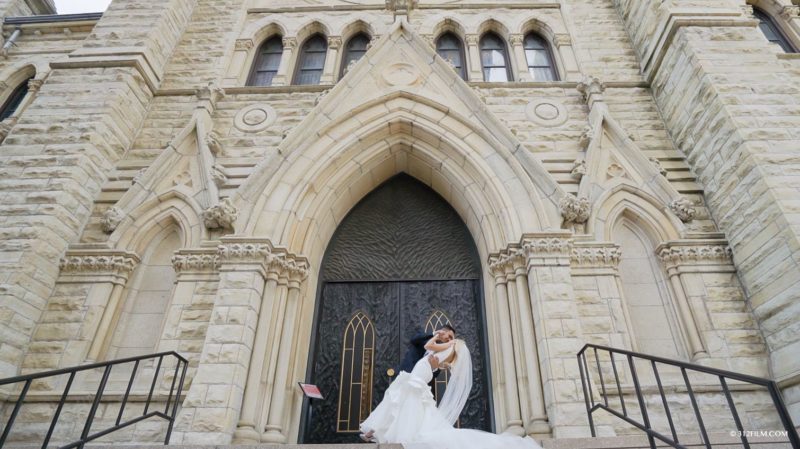 The bride and groom are standing in front of the Holy Name Cathedral in Chicago.