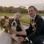 A bride and groom pose with a dog on their wedding day