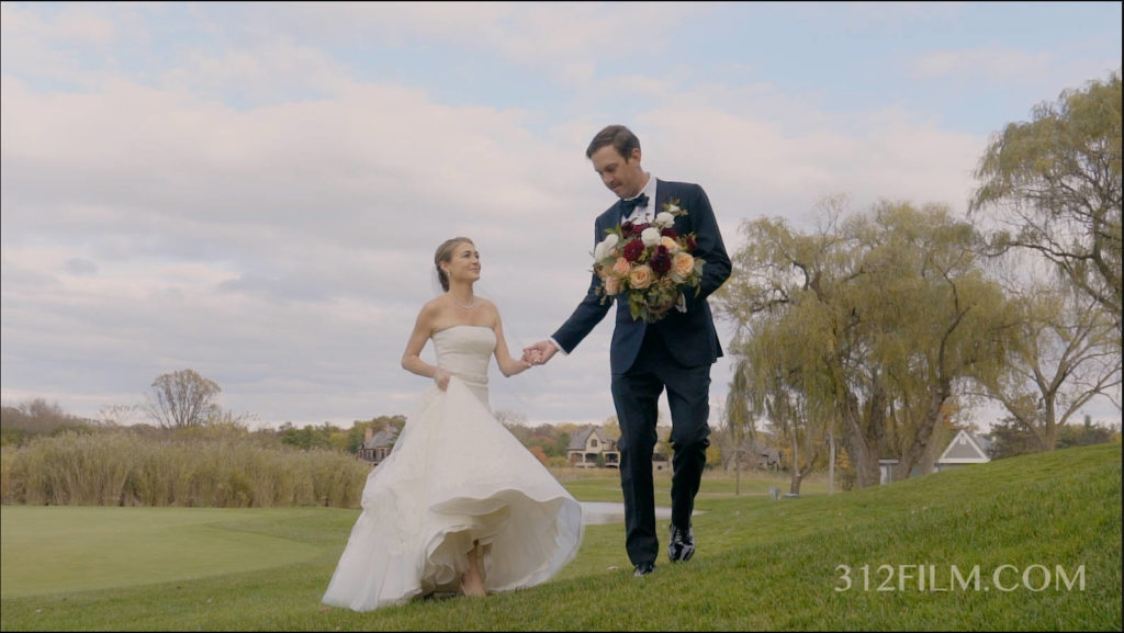 A bride and groom are walking hand in hand through a field.