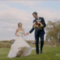 A bride and groom walking in a field holding hands