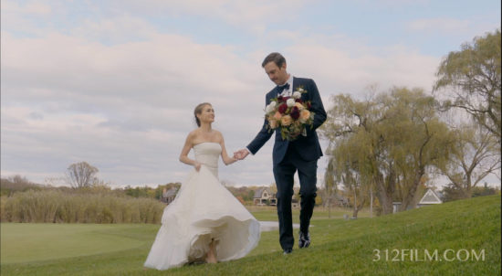A bride and groom walking in a field holding hands