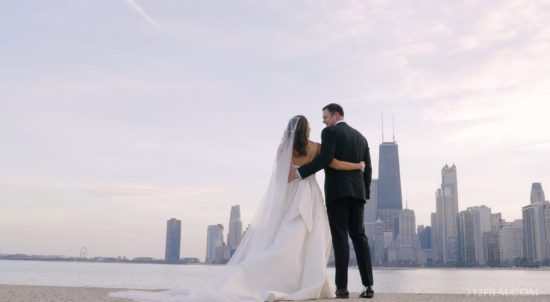 A bride and groom standing on a beach in front of a Chicago city skyline