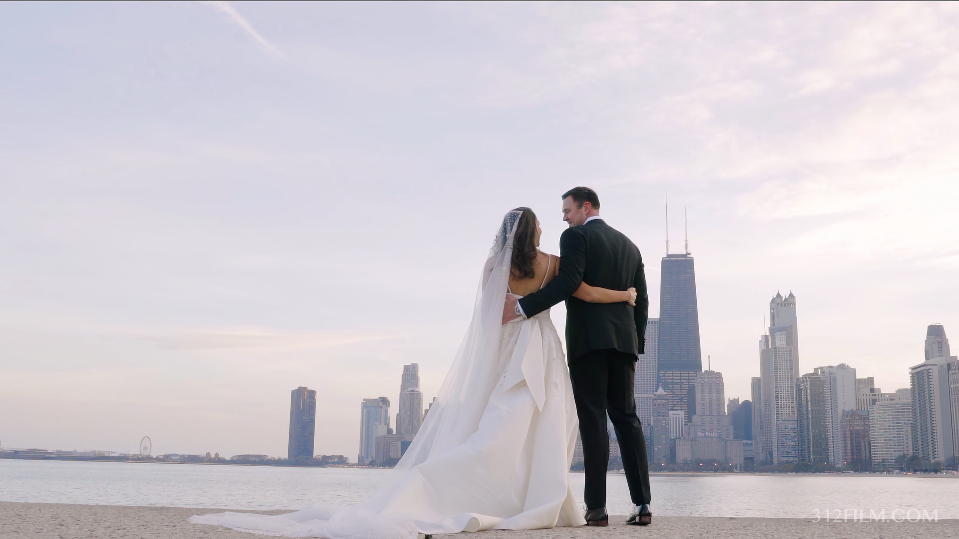 A bride and groom standing on a beach in front of a Chicago city skyline