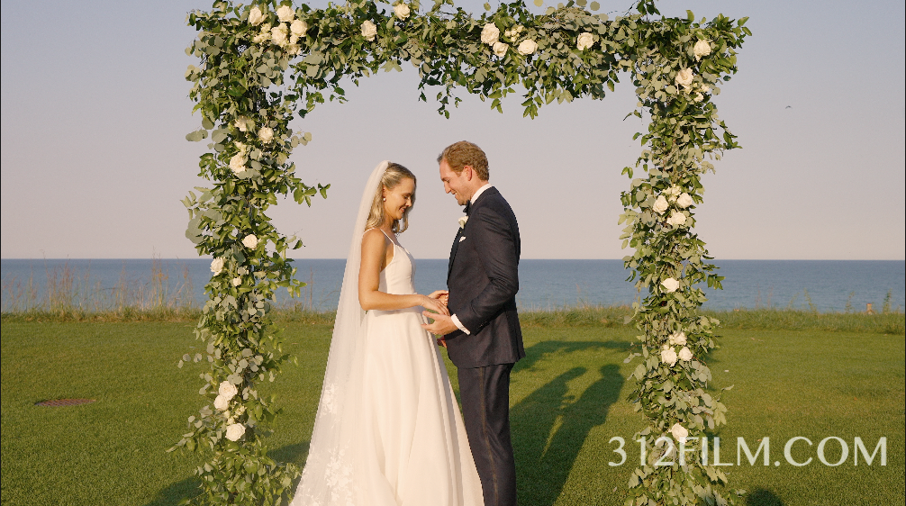 The bride and groom stand in the flower arch by the Lake Michigan lakeshore at the Lake Shore Country Club. 