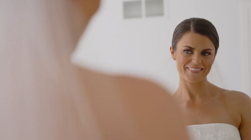 The bride looks into the mirror after Bianca Sansosti Artistry has finished doing her hair and makeup.