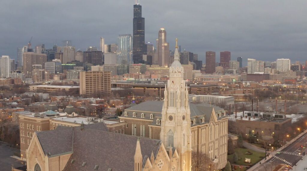 An aerial view of the Church of the Holy Family, with the city centre and the Willis Tower in the background.
