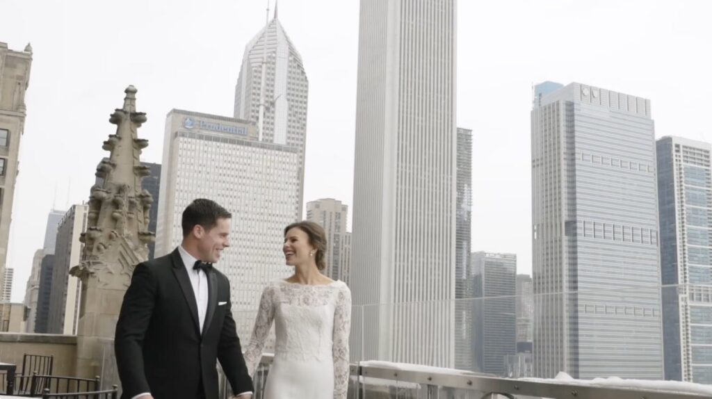 A couple walk along the balcony of the University Club of Chicago, with the city skyline in the background.